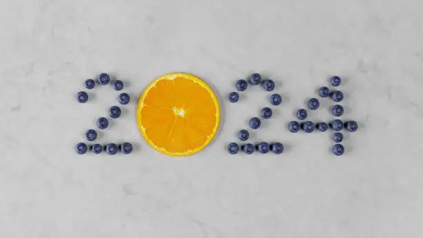 Welcome to 2024 spelled out with fresh blueberries and a bright orange on a marble countertop