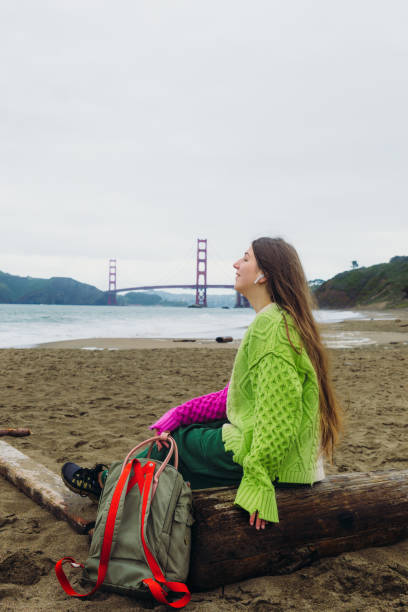 happy woman contemplating baker beach in san francisco, california listening to music - golden gate bridge audio стоковые фото и изображения