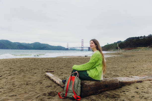 happy woman contemplating baker beach in san francisco, california listening to music - golden gate bridge audio стоковые фото и изображения