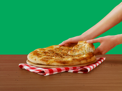 Side view of a woman removing a slice of pide; Turkish bread, in front of a green background