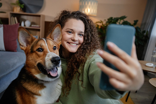 Portrait of smiling young woman taking selfie photo with happy dog at home, copy space