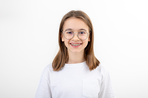 Teenage girl in a white T-shirt, glasses and braces on her teeth isolated on white.