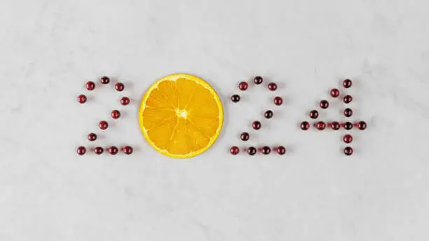 Welcome to 2024 spelled out with fresh cranberries and a bright orange on a marble countertop