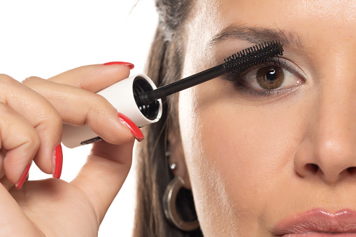 beautiful woman applying mascara on a white studio background