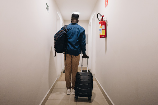Rear view of a mid adult man arriving with suitcases in apartment corridor
