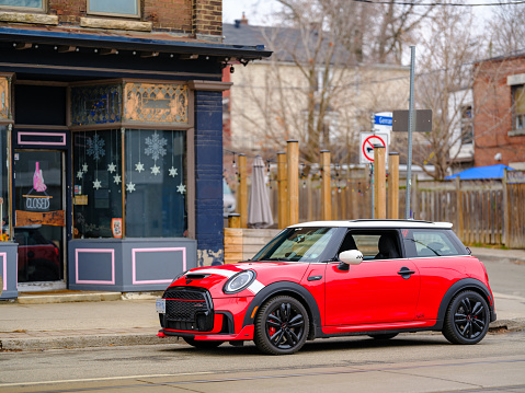 Toronto, Ontario, Canada- December 24, 2023.  Chili red colour MINI COOPER on the streets of Toronto East side, Canada. Foggy morning with overcast sky.  This is the third generation model F56 JCW, since BMW took over iconic brand of MINI. MINI featured in the photo is John Cooper Works model, the most powerful 2 door version. For the first time, this compact car features engine build and designed by BMW, and packs even more power and torque than previous models since 2002 to present. Original design clues and themes are still present on this brand new model. Mini has been around since 1959 and has been owned and issued by various car manufacturers.