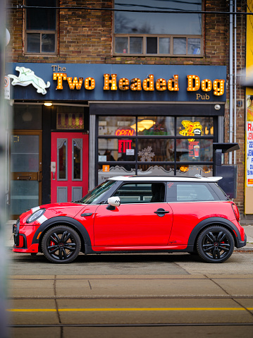 Toronto, Ontario, Canada- December 24, 2023.  Chili red colour MINI COOPER on the streets of Toronto East side, Canada. Foggy morning with overcast sky.  This is the third generation model F56 JCW, since BMW took over iconic brand of MINI. MINI featured in the photo is John Cooper Works model, the most powerful 2 door version. For the first time, this compact car features engine build and designed by BMW, and packs even more power and torque than previous models since 2002 to present. Original design clues and themes are still present on this brand new model. Mini has been around since 1959 and has been owned and issued by various car manufacturers.