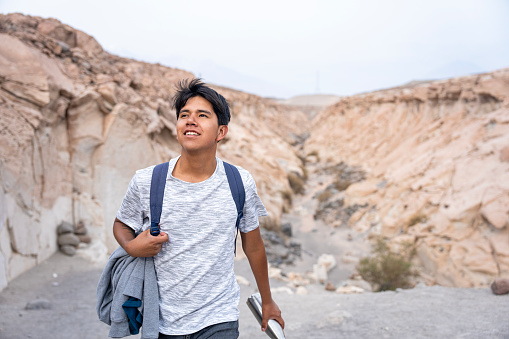 Mid-shot front view of young Peruvian man taking a walk in the desert area of Quebrada de las Culebrillas, Ruta del Sillar, Arequipa, Perú