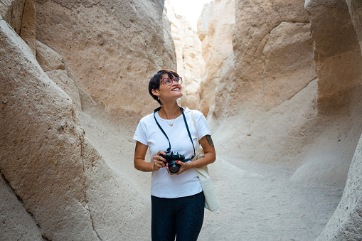 Medium shot front view of Latin woman taking photos while hiking  in Quebrada de las Culebrillas, Ruta del Sillar, Arequipa, Perú