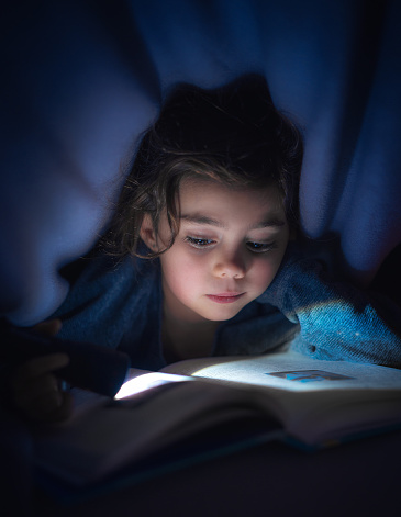 Portrait of a girl reading under the blankets with a flashlight