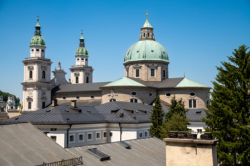 Salzburg, Salzburg - Austria â 06-17-2021: The Cathedral of Salzburg towering over other buildings in the foreground with its two towers and the roof of the cathedral against a blue sky.