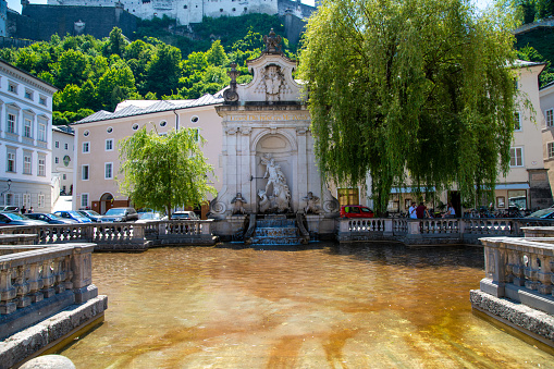 Salzburg, Salzburg - Austria â 06-17-2021: View of the Kapitelschwemme or Horse Well, a fountain in Salzburg with a figure in the center, surrounded by buildings and trees.