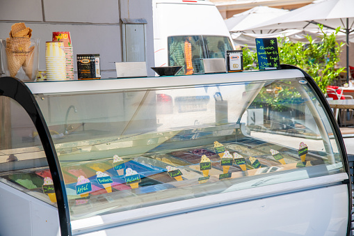 Salzburg, Salzburg - Austria - 06-17-2021: Ice stand with colorful ice cream flavors behind glass. Flavors labeled, napkins, and ice cream cones on the counter.