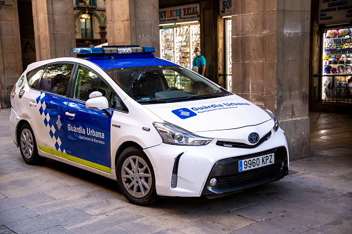 Barcelona, Catalonia, Spain - 09-02-2021: A blue and white Guardia Urbana police car parked in front of a building with a flashing blue light on the roof.