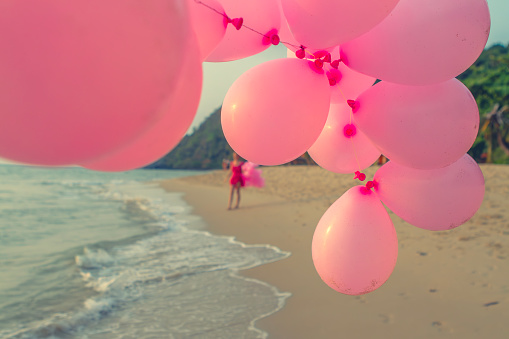 Young woman walking with big bunch o balloons in sunset