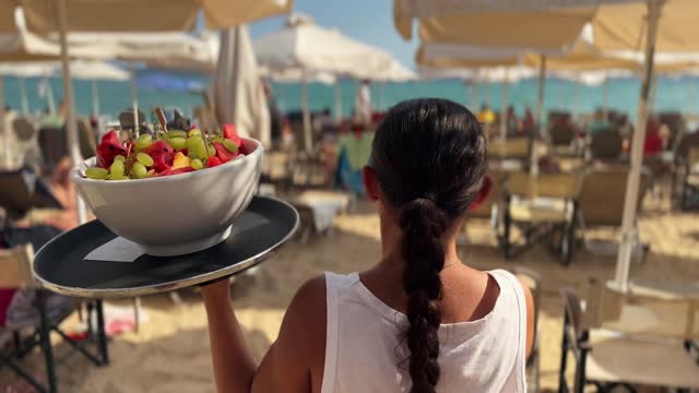 Unrecognizable waitress carrying a tray with an fruit bowl, at the beach cafe