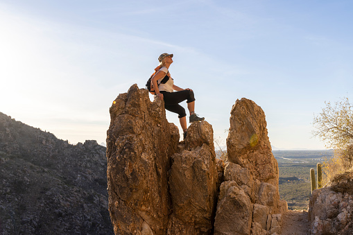 Mature woman hiker pauses on rock pinnacle above desert