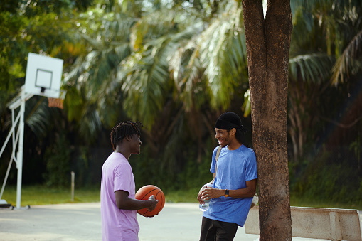 Cheerful friends talking after playing streetball in local park