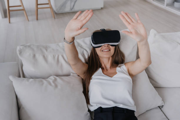 istock Excited woman experiencing virtual reality with a VR headset, lying on a sofa in a light-filled living room. 1885455886