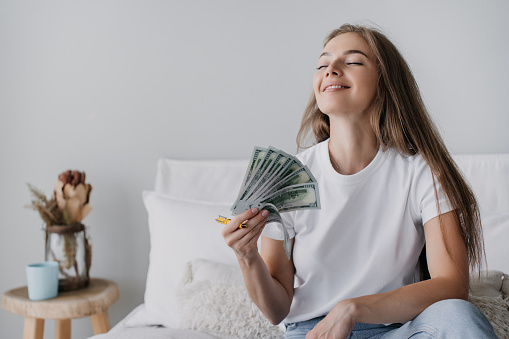 Smiling woman holding money, feeling content, sitting casually on a sofa in a cozy room with subtle decor