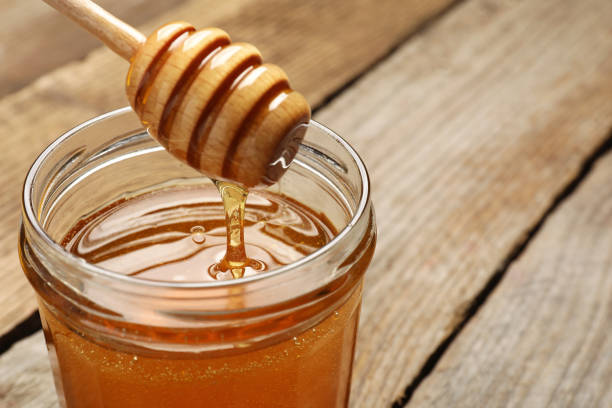 istock Pouring honey from dipper into jar on table, closeup. Space for text 1885471095
