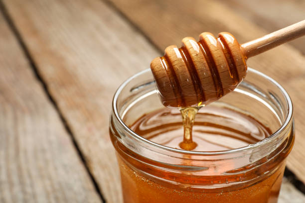 istock Pouring honey from dipper into jar on table, closeup. Space for text 1885471097