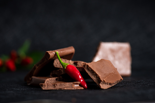 Pieces of dark milk chocolate with red pepper on a black background