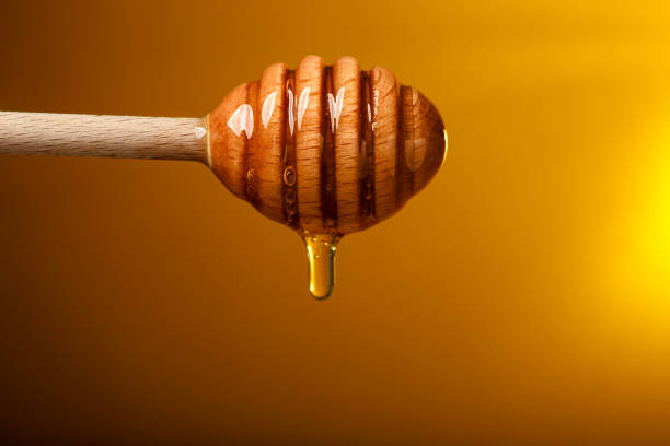 istock Pouring honey from dipper against golden background, space for text 1885472139