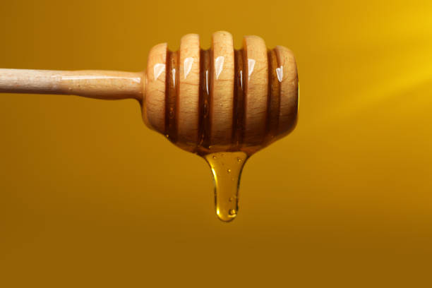 istock Pouring honey from dipper against golden background, closeup 1885472857