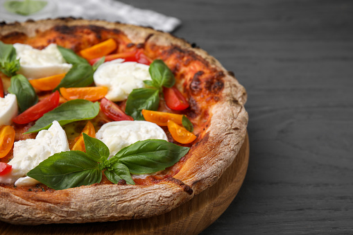 Delicious pizza with burrata cheese, tomatoes and basil on grey wooden table, closeup. Space for text