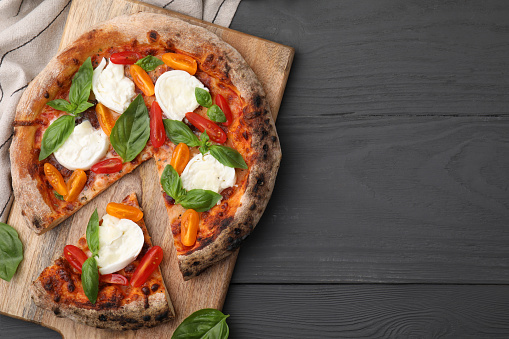 Delicious pizza with burrata cheese, tomatoes and basil on grey wooden table, top view. Space for text