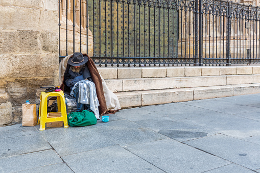 Seville, Spain - December 20, 2023: An old beggar sits in front of the Seville cathedral
