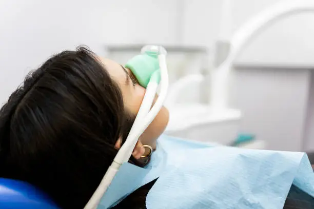 An adult woman sits in a dentist's clinic wearing a nasal mask to inhale nitrous oxide. Dentist fear concept. Feeling of relaxation with laughing gas.