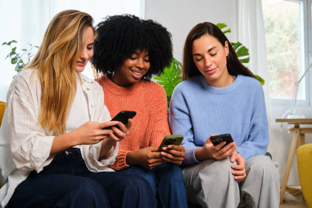 Group of three young female flat mates using the smartphone at home. stock photo