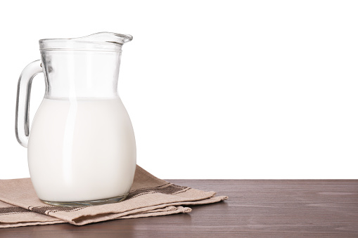 Jug of tasty milk on wooden table against white background