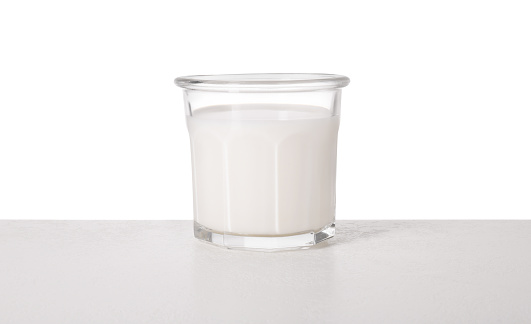 Glass of tasty milk on light table against white background