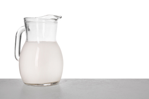 Jug of tasty milk on light table against white background