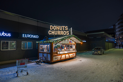 Sweden. Uppsala. 12.23.2023. Close-up view of a street kiosk selling donuts and churros illuminated on a winter evening.