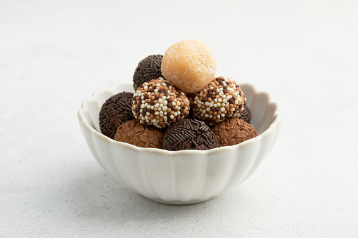 Typical Brazilian sweet brigadeiro, based on condensed milk. A heap of assorted flavors of candies in a white ceramic bowl on a white table