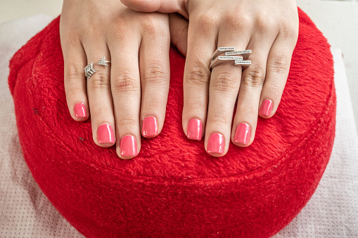 Manicure in a beauty salon, where the result of the work done is shown. Woman's hands with rings and bracelet on a red cushion.
