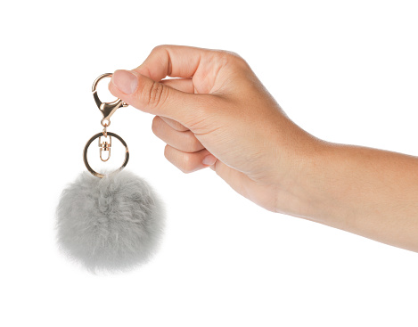 Woman holding gray faux fur keychain on white background, closeup