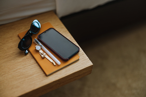 Close Up of a Mobile Phone, Sunglasses and a Watch on the Bedside Table (Copy Space)