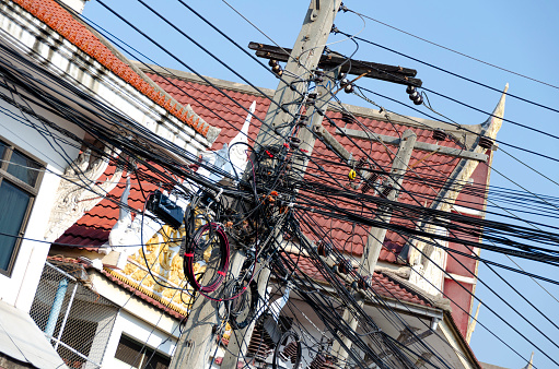 An image capturing the intricate network of overhead electrical cables and wires in Bangkok, a complex web that epitomizes the city's rapid urban growth and development. This tangle of lines against the urban backdrop highlights the bustling energy and infrastructure of Thailand's capital city.