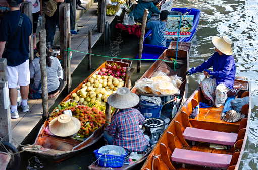 29th January, 2016 - Bangkok, Thailand: Bustling with activity, the floating market in Bangkok is a vibrant mosaic of colors and sounds. Market traders skillfully navigate their boats, laden with a variety of local produce and goods, while boat excursion operators guide tourists and local buyers through the waterways. The scene is a lively showcase of traditional Thai commerce and culture, with visitors engaging in the unique experience of shopping on water.