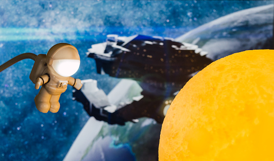 Little toy astronaut traveling through space and reaching the moon, with a background of a spaceship and space