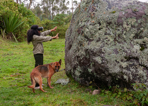 afro girl with augmented reality glasses getting information about a prehistoric stone thanks to advanced technology together with her earless dog. High quality photo