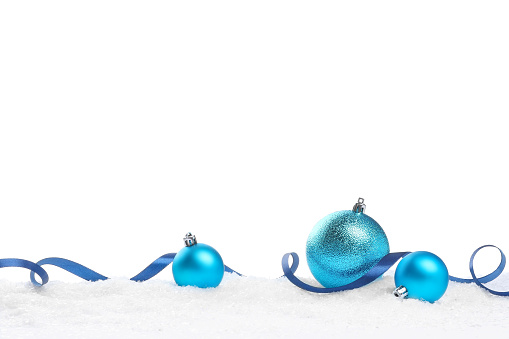 Beautiful light blue Christmas balls and ribbon on snow against white background