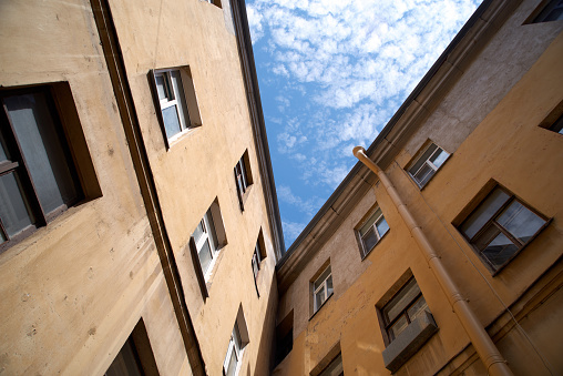 View from below of old square courtyard well in St. Petersburg, Russia. Wall, windows and part of blue sky