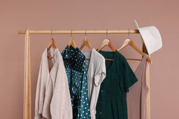 istock Rack with hat and stylish women`s clothes on wooden hangers against beige background 1885669607