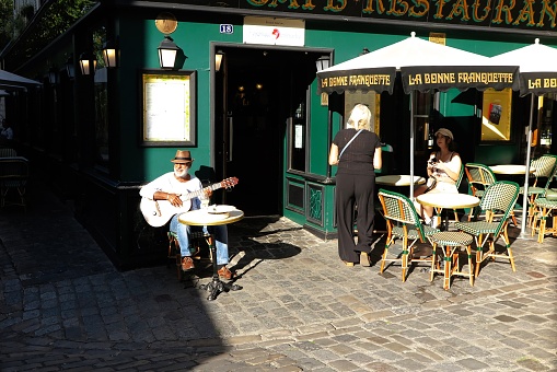 Paris, France - Oct. 2, 2023:  A street musician plays guitar for contributions at a sidewalk cafe in the Montmartre district.